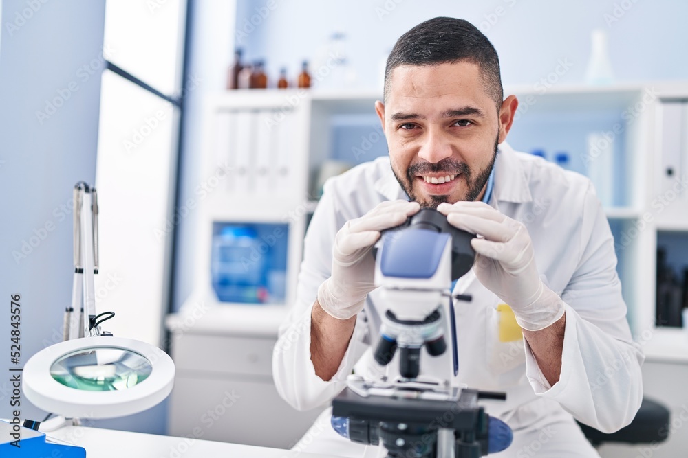 Young latin man scientist smiling confident using microscope at laboratory Young latin man scientist smiling confident using microscope at laboratory