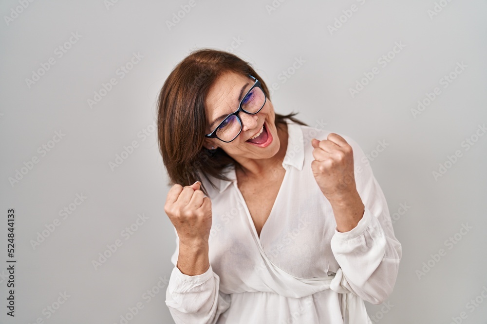 Middle age hispanic woman standing over isolated background very happy and excited doing winner gesture with arms raised, smiling and screaming for success. celebration concept. Middle age hispanic woman standing over isolated background very happy and excited doing winner gesture with arms raised, smiling and screaming for success. celebration concept.