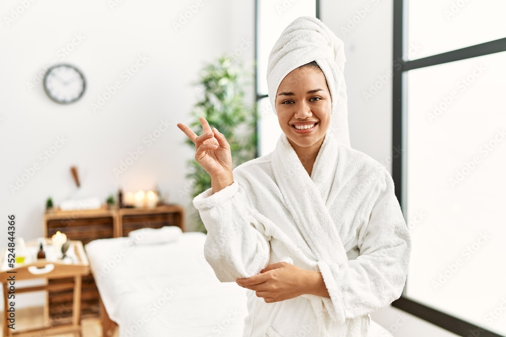 Young brunette woman wearing towel and bathrobe standing at beauty center smiling with happy face winking at the camera doing victory sign. number two. Young brunette woman wearing towel and bathrobe standing at beauty center smiling with happy face winking at the camera doing victory sign. number two.