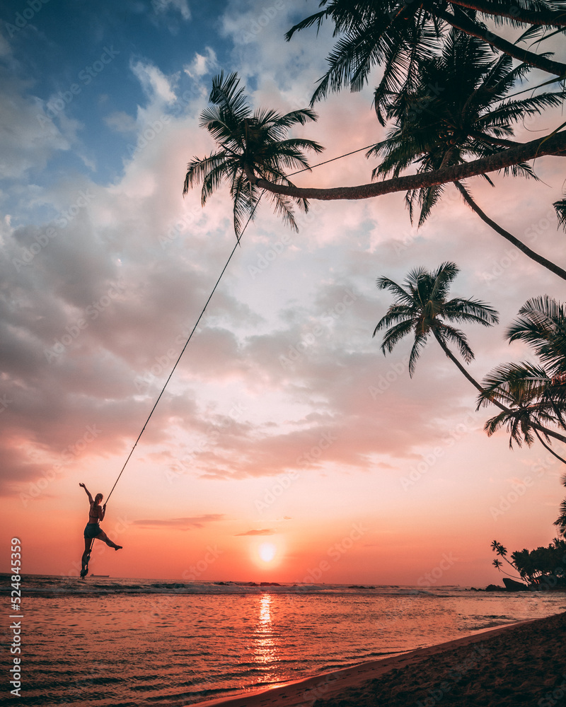 a tourist on a palm swing in Unawatuna, Sri Lanka during sunset