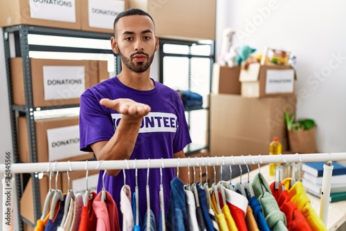 African american man wearing volunteer t shirt at donations stand looking at the camera blowing a kiss with hand on air being lovely and sexy. love expression.
