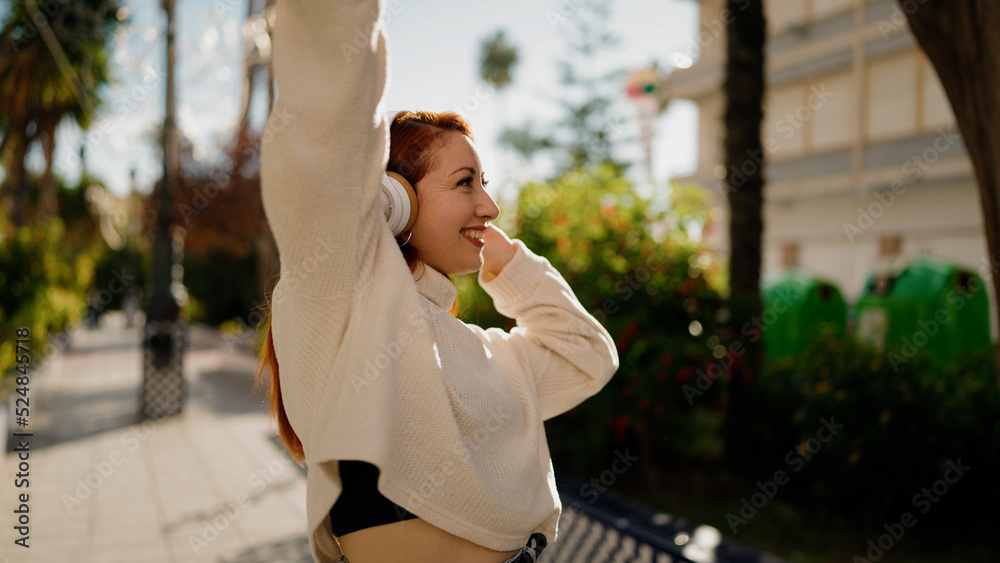 Young redhead woman listening to music and dancing at park