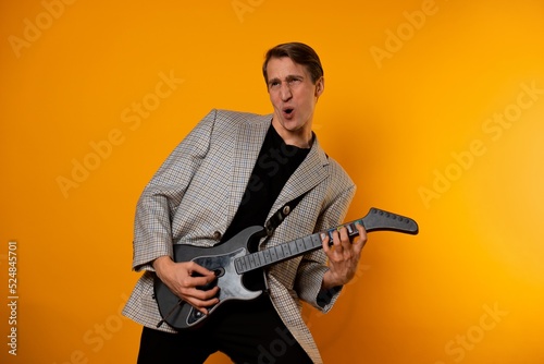 rock ' n ' roll guy, a cool guy with a fake guitar, pretends to play music. Fun and emotion. A guy in a jacket with a gaming guitar, playing guitar in a simulator photo