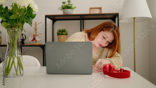 Young redhead woman using laptop sitting on desk at home