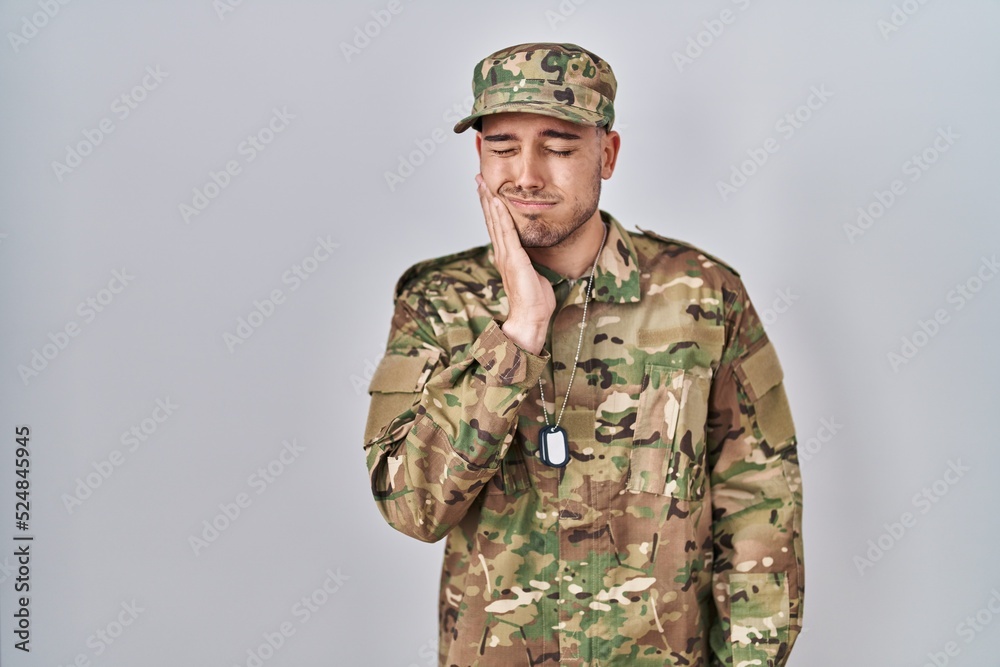 Young hispanic man wearing camouflage army uniform touching mouth with hand with painful expression because of toothache or dental illness on teeth. dentist Young hispanic man wearing camouflage army uniform touching mouth with hand with painful expression because of toothache or dental illness on teeth. dentist