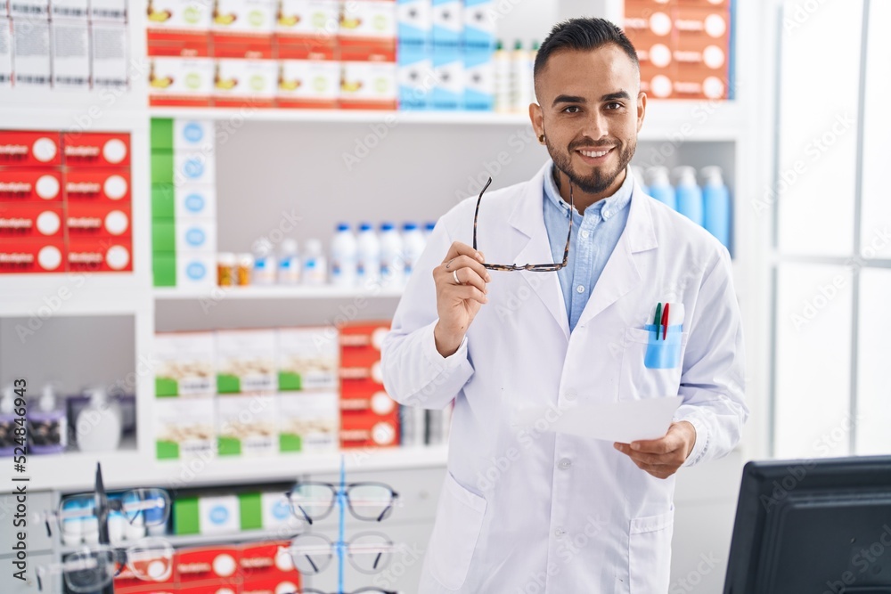 Young hispanic man pharmacist holding prescription working at pharmacy Young hispanic man pharmacist holding prescription working at pharmacy