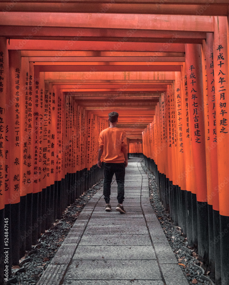 a tourist walking through the famous torii gates of the Fushimi Inari Shrine in Kyoto, Japan - obrazy, fototapety, plakaty 