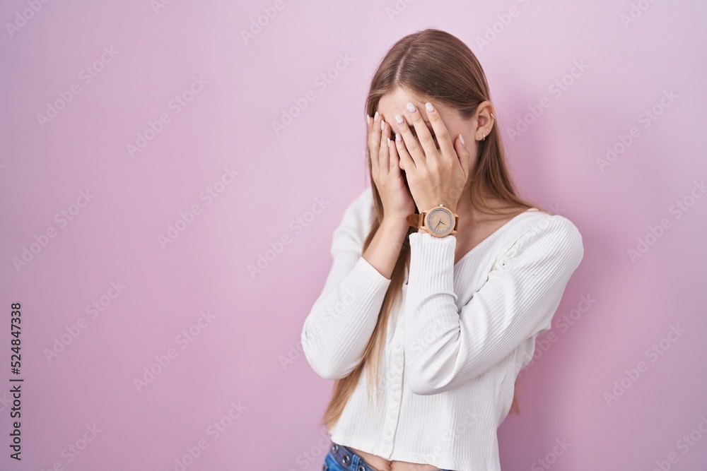 Young caucasian woman standing over pink background with sad expression covering face with hands while crying. depression concept. Young caucasian woman standing over pink background with sad expression covering face with hands while crying. depression concept.