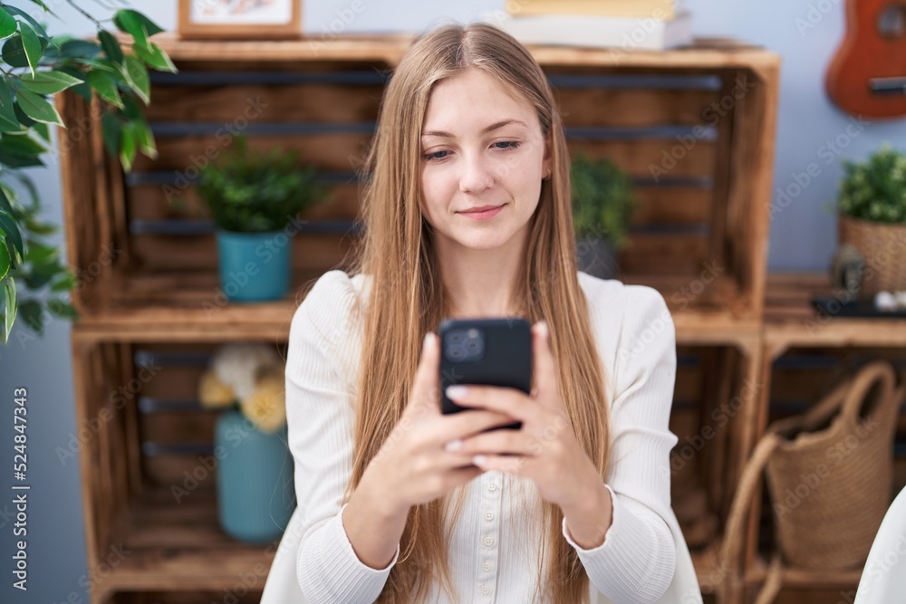 Young caucasian woman using smartphone sitting on table at home