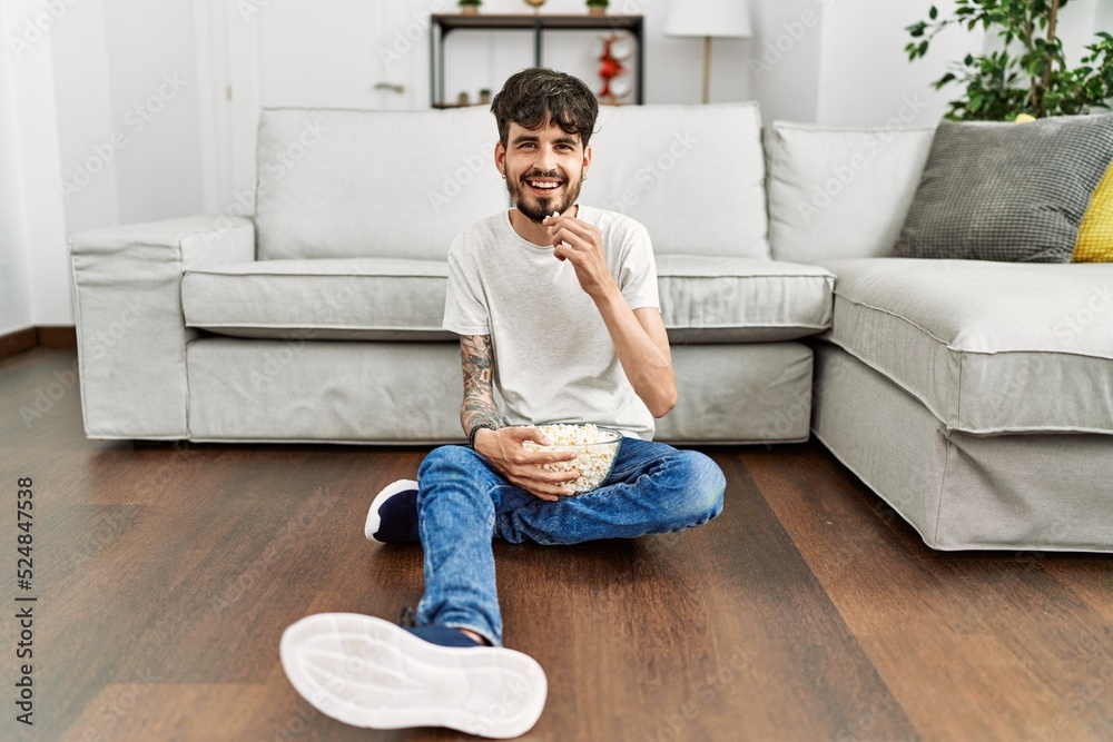 Young hispanic man watching movie sitting on the floor at home. Young hispanic man watching movie sitting on the floor at home.