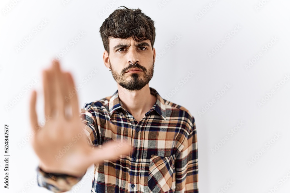 Hispanic man with beard standing over isolated background doing stop sing with palm of the hand. warning expression with negative and serious gesture on the face. Hispanic man with beard standing over isolated background doing stop sing with palm of the hand. warning expression with negative and serious gesture on the face.