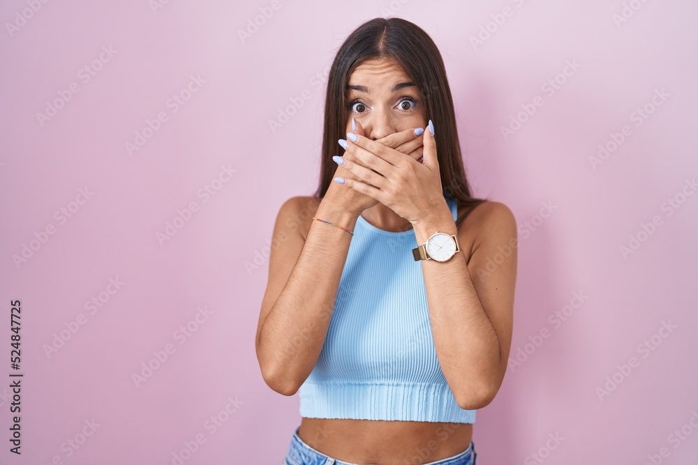 Young brunette woman standing over pink background shocked covering mouth with hands for mistake. secret concept. Young brunette woman standing over pink background shocked covering mouth with hands for mistake. secret concept.