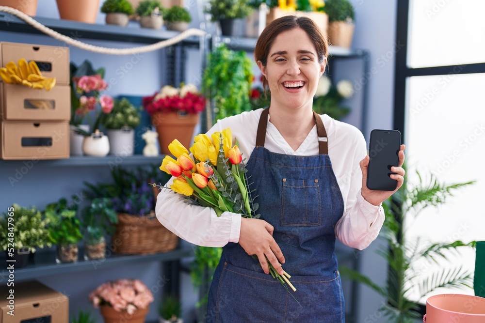 Brunette woman working at florist shop holding smartphone smiling and laughing hard out loud because funny crazy joke.