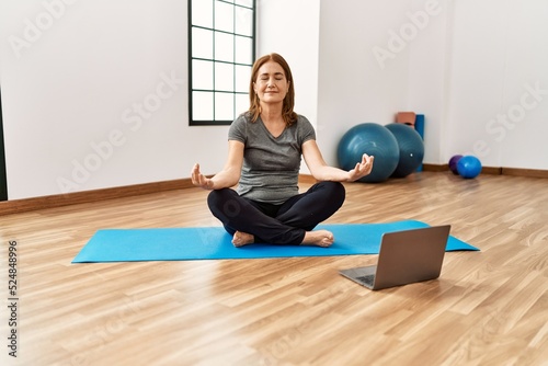 Middle age caucasian woman smiling confident having online yoga class at sport center