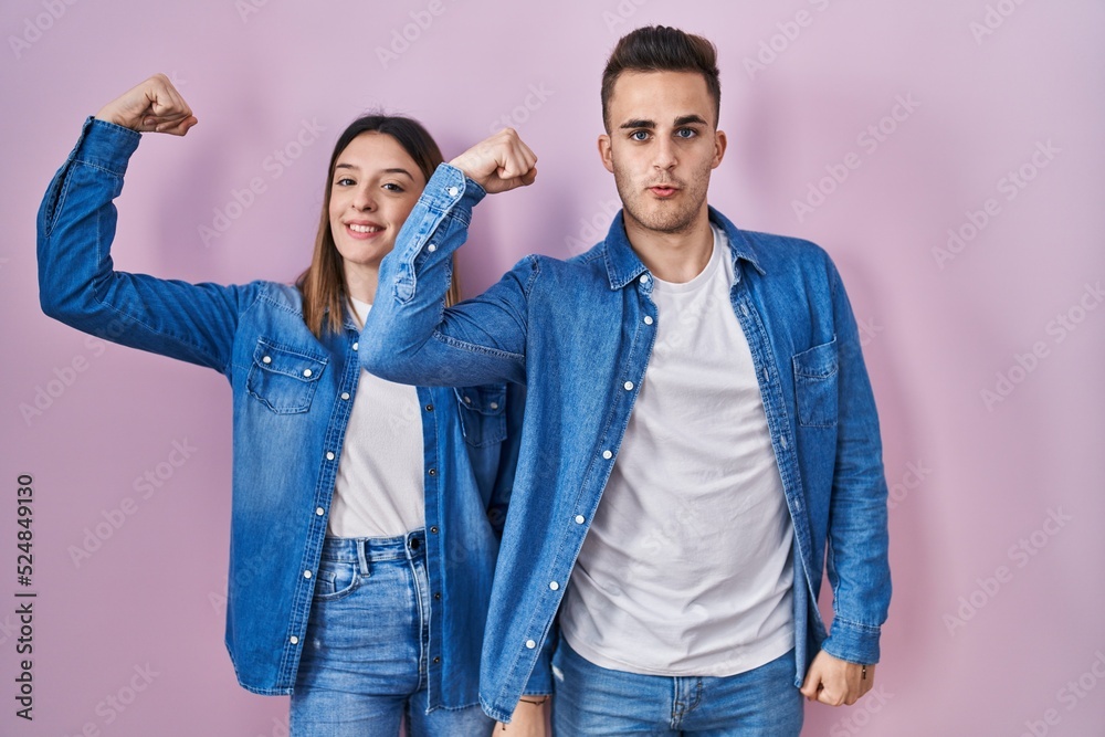Young hispanic couple standing over pink background strong person showing arm muscle, confident and proud of power Young hispanic couple standing over pink background strong person showing arm muscle, confident and proud of power