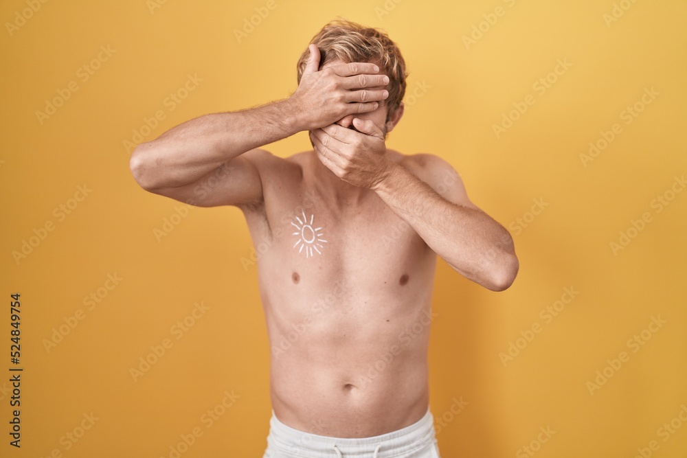 Caucasian man standing shirtless wearing sun screen covering eyes and mouth with hands, surprised and shocked. hiding emotion