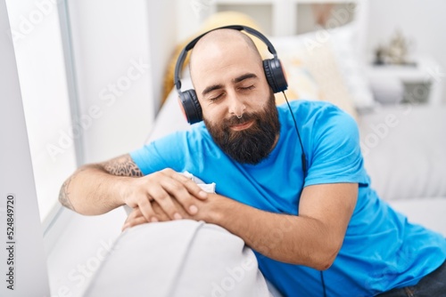Young bald man listening to music sitting on sofa at home