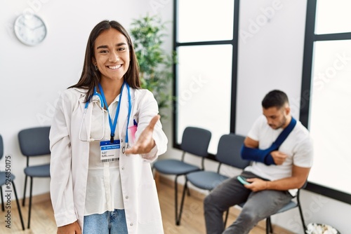 Young asian doctor woman at waiting room with a man with a broken arm smiling friendly offering handshake as greeting and welcoming. successful business.