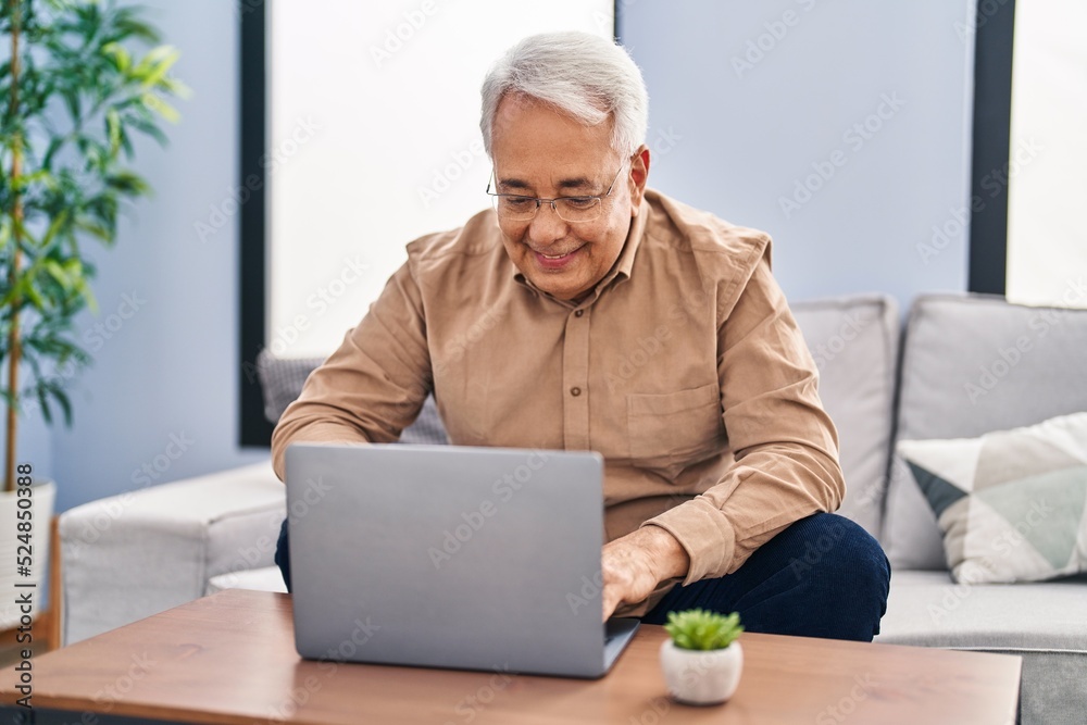 Senior man using laptop sitting on sofa at home Senior man using laptop sitting on sofa at home