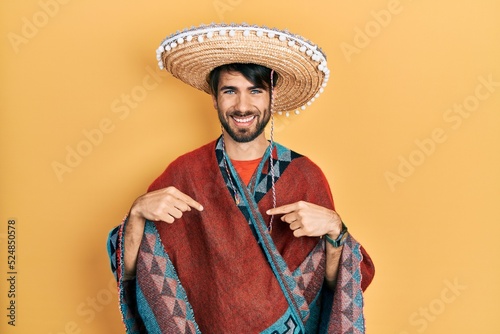 Young hispanic man holding mexican hat looking confident with smile on face, pointing oneself with fingers proud and happy.
