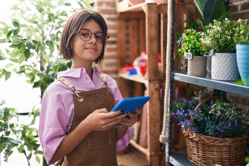 Adorable hispanic girl florist smiling confident using touchpad at flower shop