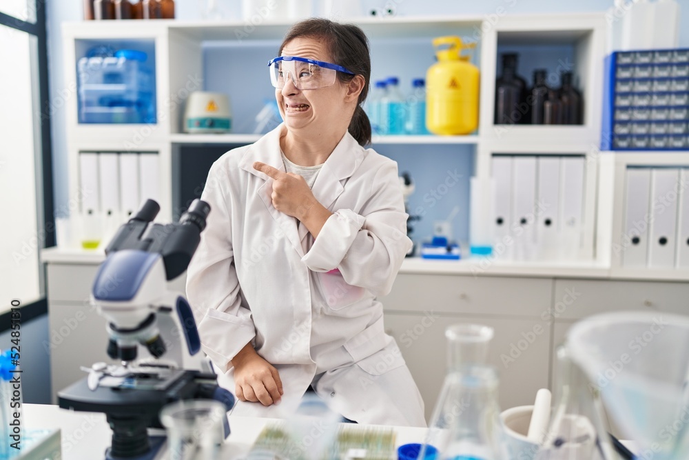 Hispanic girl with down syndrome working at scientist laboratory pointing aside worried and nervous with forefinger, concerned and surprised expression Hispanic girl with down syndrome working at scientist laboratory pointing aside worried and nervous with forefinger, concerned and surprised expression