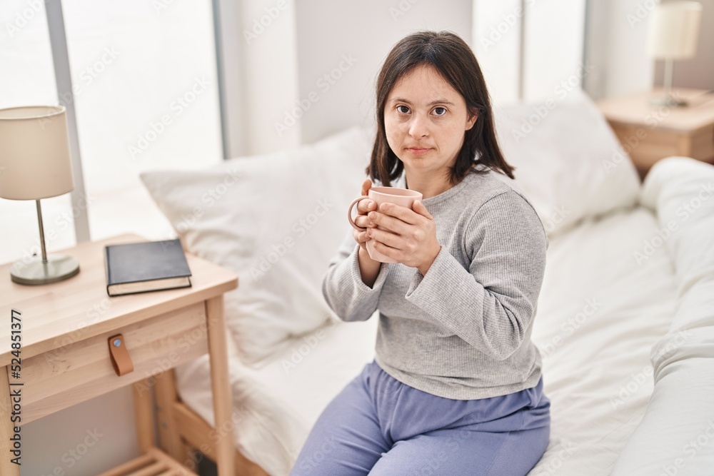 Young woman with down syndrome drinking cup of coffee sitting on bed at bedroom Young woman with down syndrome drinking cup of coffee sitting on bed at bedroom