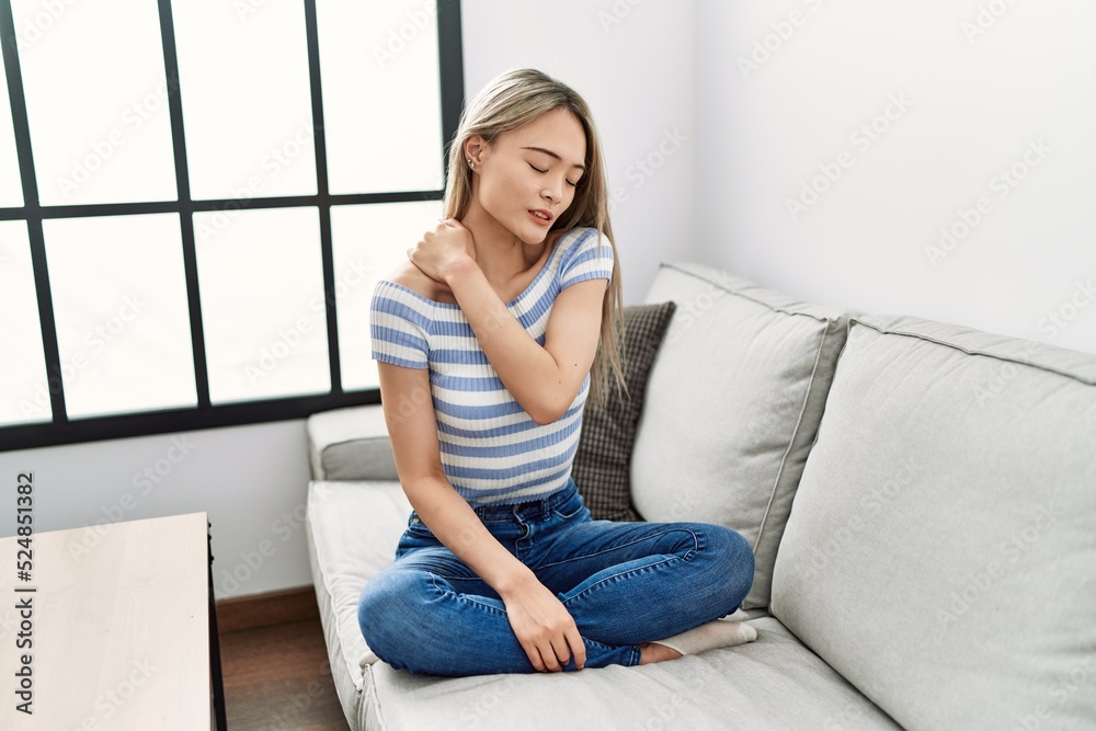 Young chinese woman with neck pain sitting on the sofa at home Young chinese woman with neck pain sitting on the sofa at home