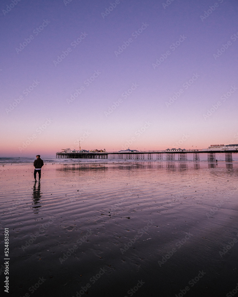 Fototapeta premium a man walking towards the Pier in Brighton, United Kingdom during sunrise