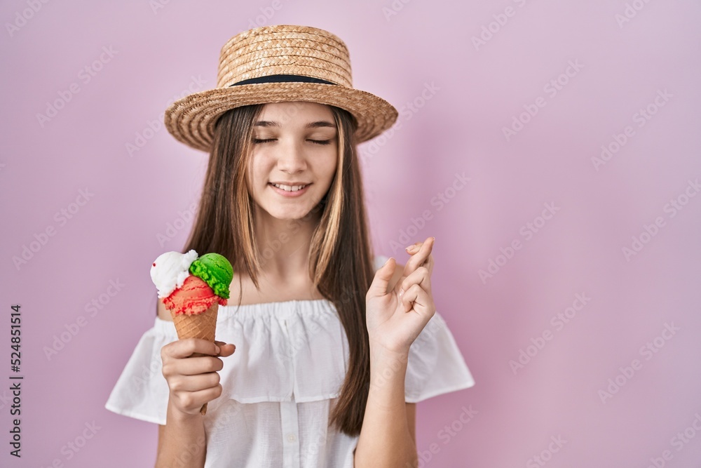 Teenager girl holding ice cream gesturing finger crossed smiling with hope and eyes closed. luck and superstitious concept.