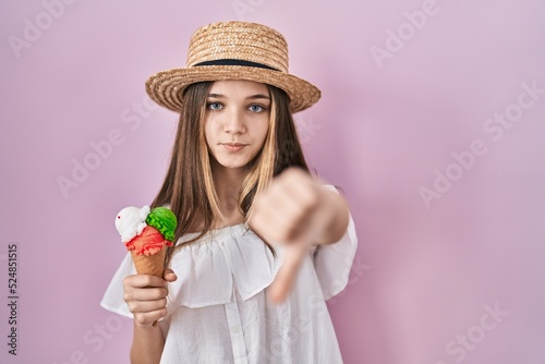 Teenager girl holding ice cream looking unhappy and angry showing rejection and negative with thumbs down gesture. bad expression.