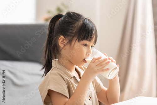 Happy Asian Kid drinking fresh milk for good health at home.Enjoy and tasty for strong bone.Female kid drink soy milk from glass tasty and delicious with calcium.Healthy Lifestyle Concept