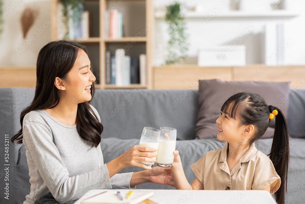 Asian mother and her daughter clink glasses enjoy and smile with milk drink.Mom and little girl holding milk glasses and drink to get calcium.Healthy Eating Concept Asian mother and her daughter clink glasses enjoy and smile with milk drink.Mom and little girl holding milk glasses and drink to get calcium.Healthy Eating Concept