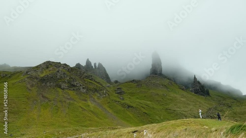 A group of rock formations beneath the mountains, immersed in heavy fog. some distant unrecognized people are visible, taking pictures and enjoying the view. 4K video clip, old man of storr, Scotland. photo