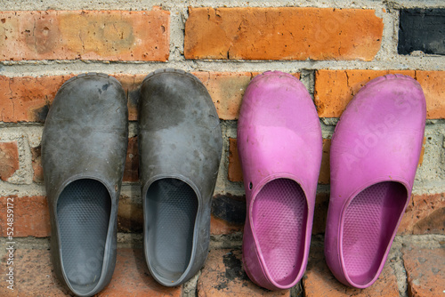 Two pairs of rubber galoshes in black and pink on the background of an old brick wall