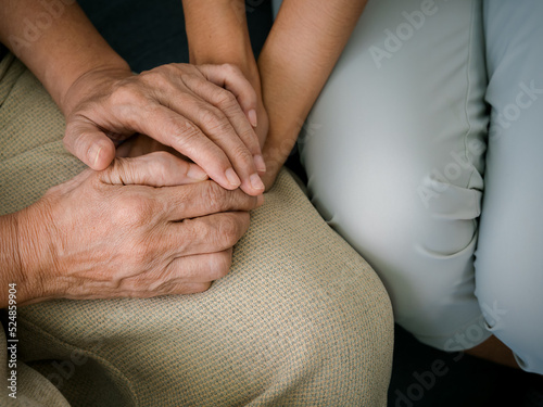 Close up of old mother, grandmother, elder or senior woman's hands hold her daughter or grandchild's hands for support with care and comfort. Giving love and encouragement concept.