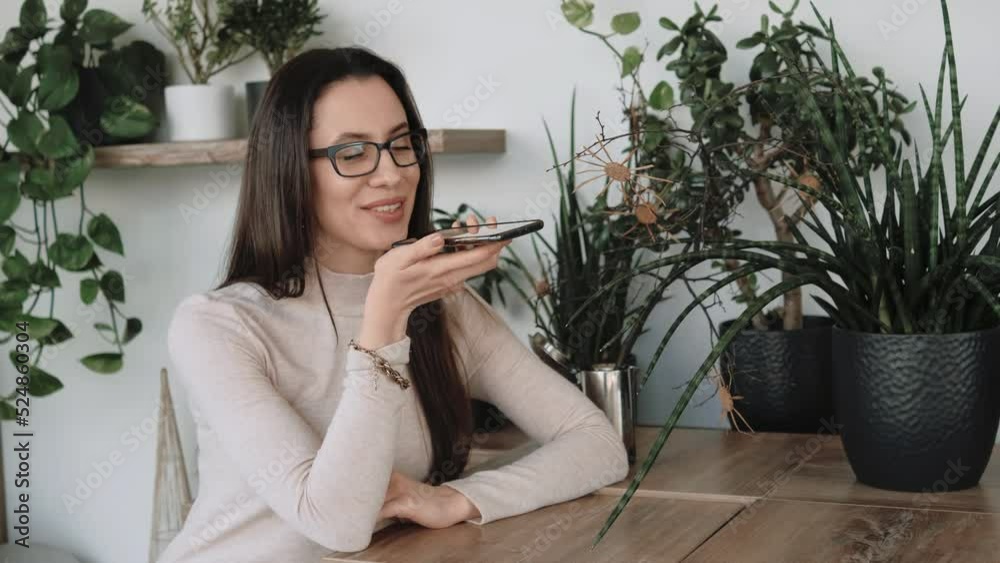 Young woman sending audio message sitting in cafe with a lot of plants n background