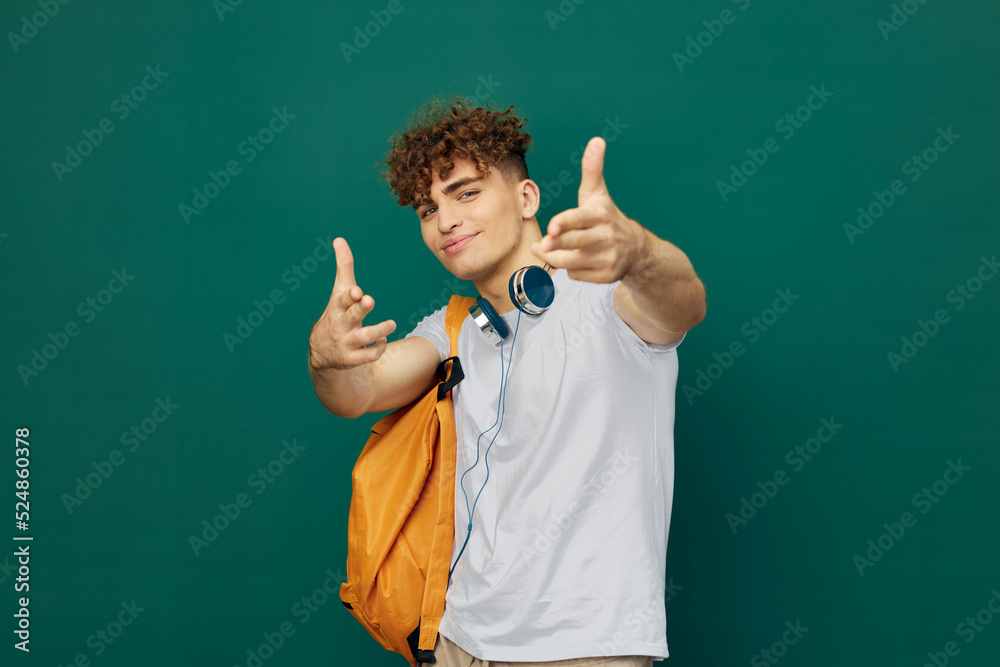 a close horizontal portrait of a handsome man with curly hair standing on a green background holding headphones around his neck and holding out his hands to the camera