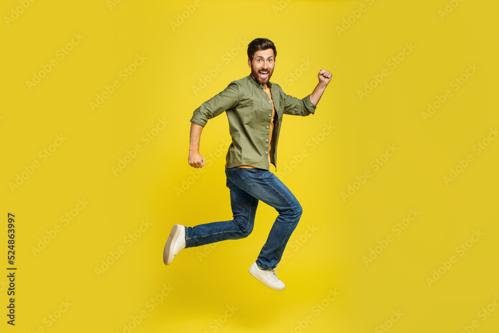 Portrait of middle aged man running over yellow background, side view shot of joyful male jumping in air