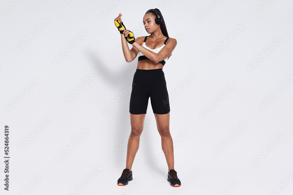 Confident young African woman in sports clothing wearing gloves against white background Confident young African woman in sports clothing wearing gloves against white background