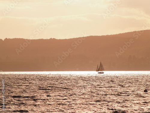 Silhouette distant hills and yacht sailing in under red sky at sunset © Brian Scantlebury