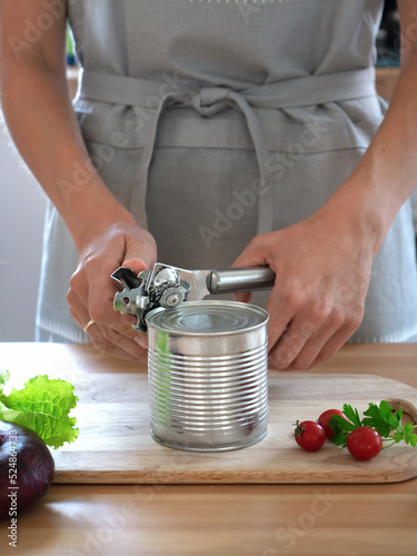 woman opens a can of canned food with a can opener in the kitchen photo