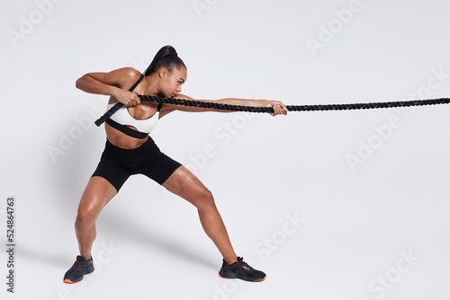 Concentrated young African woman pulling a rope against white background