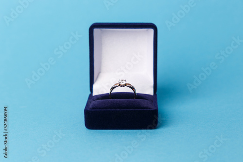 Jewelry, gold diamond ring in a blue box on a turquoise background, isolated.  A ring for a marriage proposal. Close-up. Front view. A place for your text.