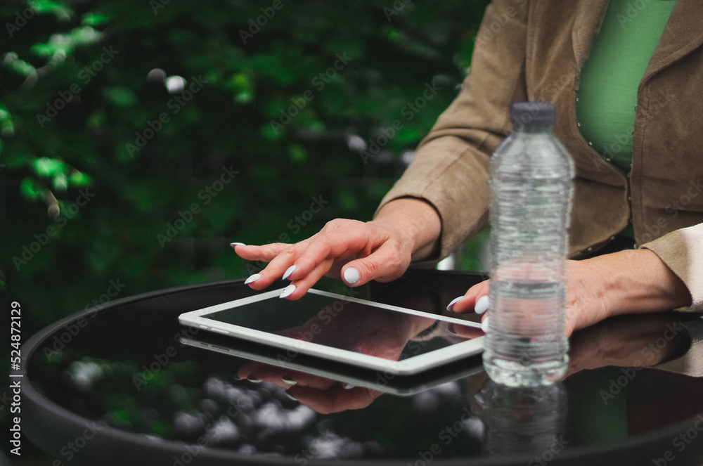 Hands of a young caucasian woman typing on the black screen of the tablet while sitting at a table