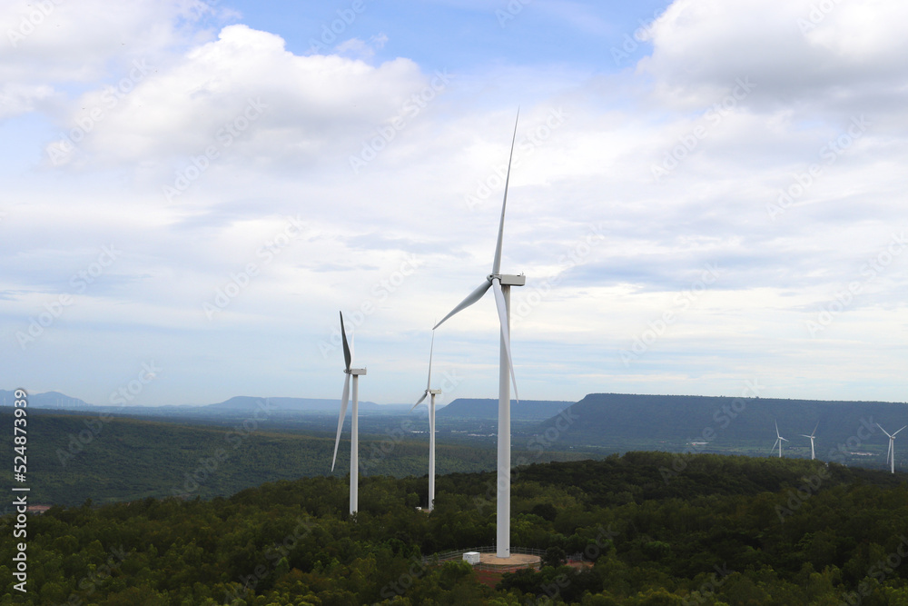 Aerial photo of a nice windmill in green forest and mountain with white clouds in the blue sky. Wind turbines for electric power with clean and Renewable Energy concept.