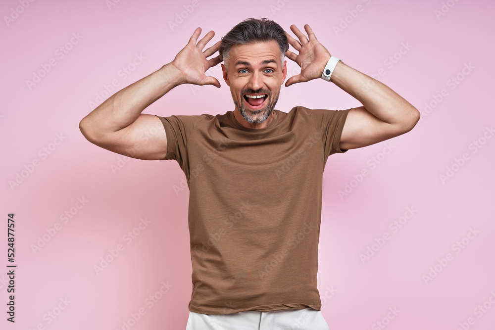 Surprised mature man looking at camera and gesturing while standing against pink background Surprised mature man looking at camera and gesturing while standing against pink background