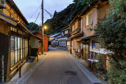 Buildings line deserted road through quiet Japanese village at dusk