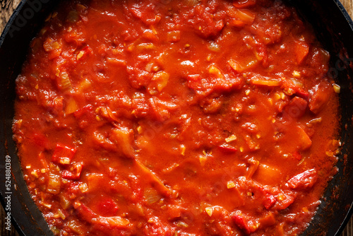 The stage of preparing a traditional shakshouka dish, slowly stewing chopped onion, garlic, pepper and tomatoes in olive oil with the addition of aromatic spices, close-up view photo