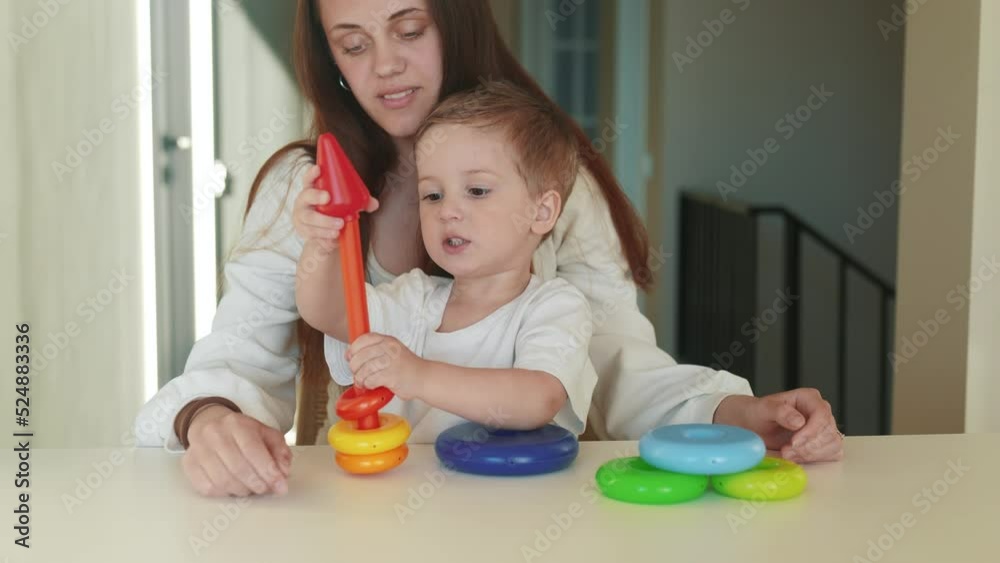 the child collects a toy pyramid. mom plays with son at home happy family. development of fine motor skills in a newborn child. happy family mom and baby play pyramid game fun. preschool education the child collects a toy pyramid. mom plays with son at home happy family. development of fine motor skills in a newborn child. happy family mom and baby play pyramid game fun. preschool education